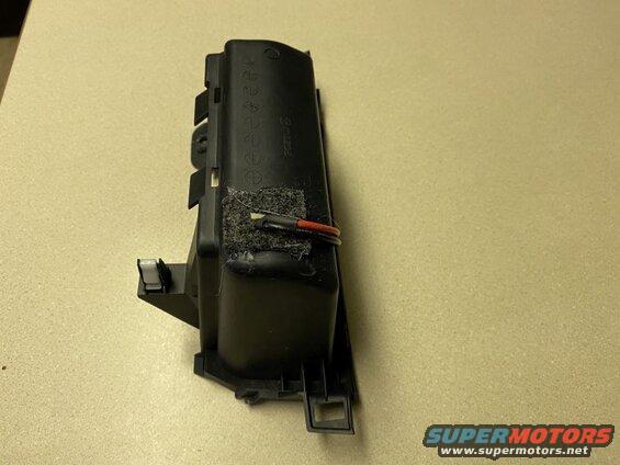 Black plastic automotive part with wires attached, on a speckled surface.