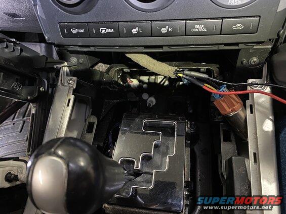 Car interior center console with gear shifter and exposed wires.