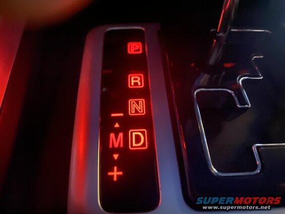 Close-up of a car's automatic transmission shifter with illuminated P, R, N, M, D selections.