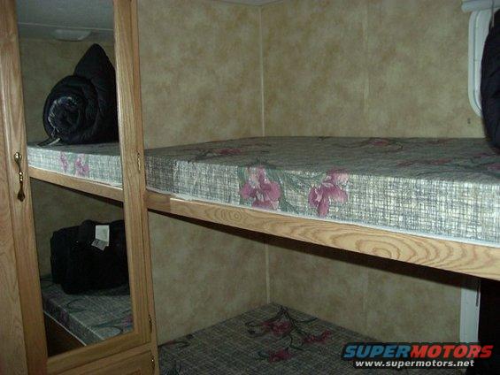 Bunk beds with floral patterned mattresses inside an RV, one mattress has a rolled sleeping bag on it
