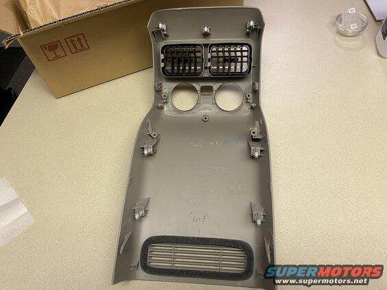 Tan plastic center console trim piece with air vents and mounting clips.