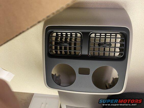 Rear climate control vents and cup holders in a car interior.