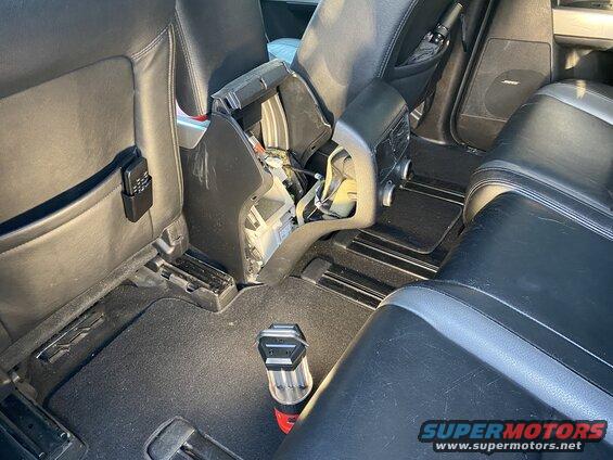 Interior back seat of a vehicle with center console removed, black leather seats, and a flashlight on the floor.