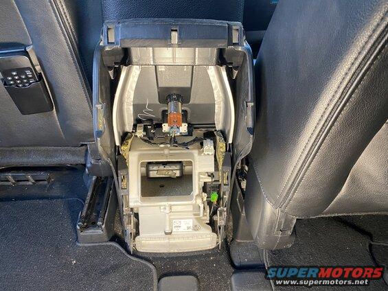 Disassembled center console in a vehicle, showing wiring and internal parts between black leather seats.