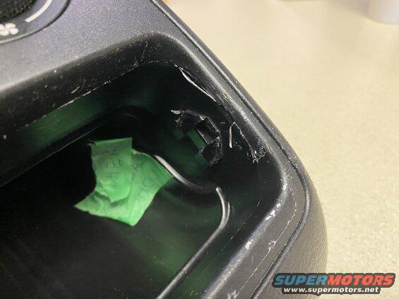 Close-up of damaged black plastic interior trim in a vehicle's center console with green tape.