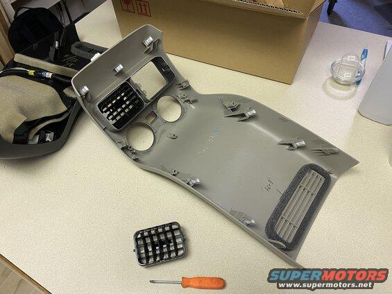 Disassembled gray center console trim piece with air vents and screwdriver on a countertop.