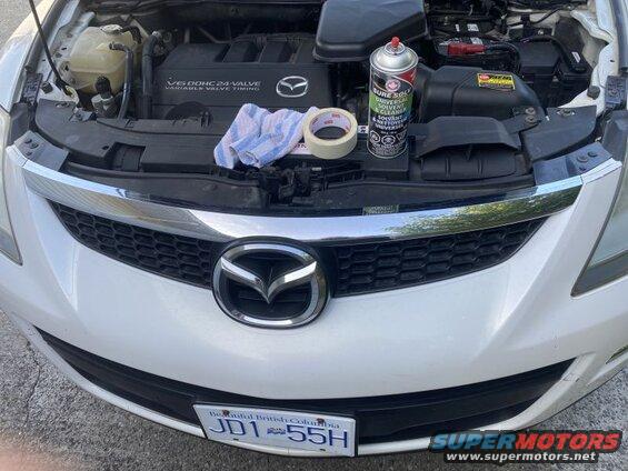White 2009 Mazda CX-9 front view, hood open, engine bay with cleaning supplies.