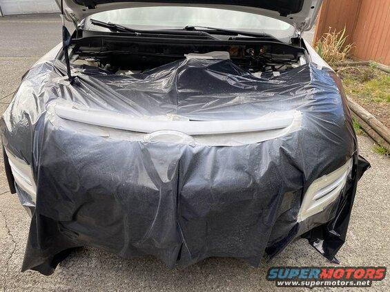Front of a white SUV covered in black plastic, hood open.