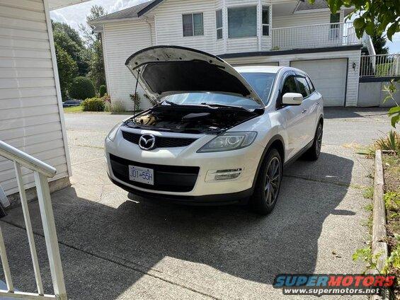 White 2009 Mazda CX-9 SUV with hood open, parked in driveway.