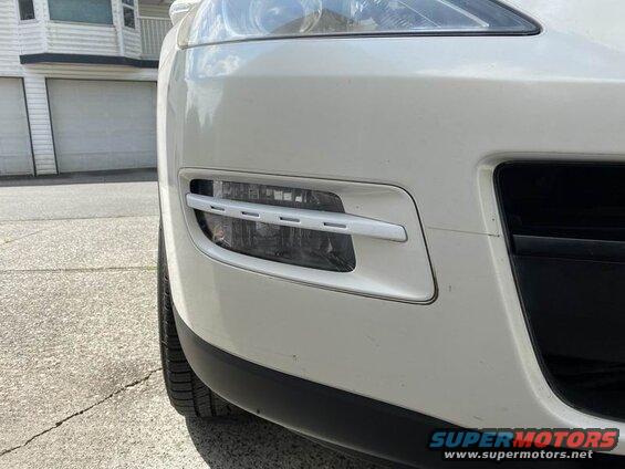 White SUV front bumper and headlight assembly. Parked on concrete driveway.
