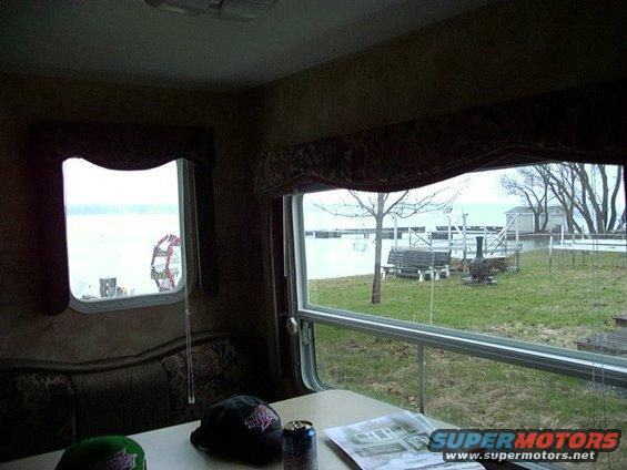 Interior of an RV with a table, caps, and a can, looking out a window at a lake and trees
