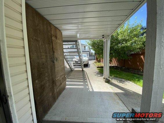 Exterior shot of a covered walkway with a wooden door and metal stairs.