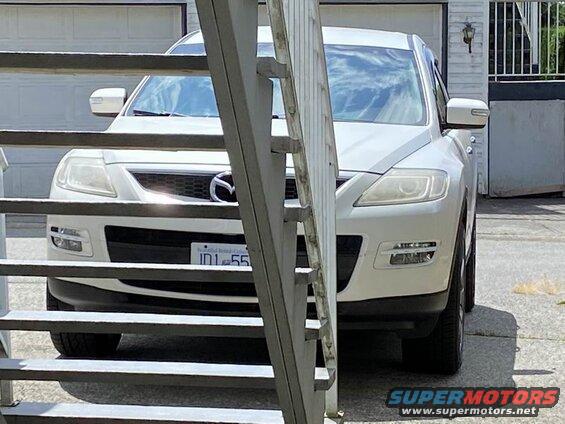 White Mazda CX-9 front view, partially obscured by a metal railing.