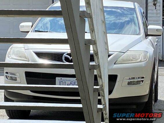 Front view of a white Mazda CX-9 SUV behind metal railings, with a British Columbia license plate.