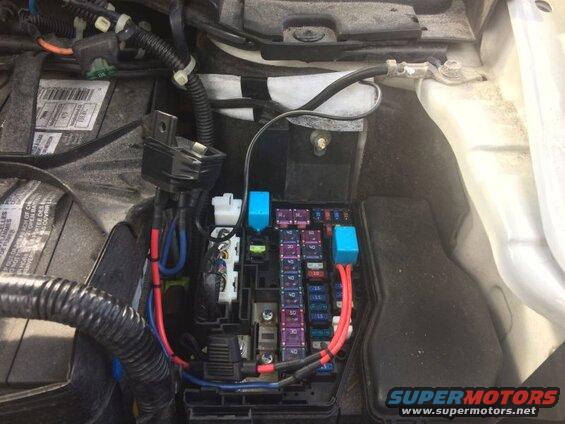 Vehicle engine bay showing battery, fuse box, and wiring modifications.