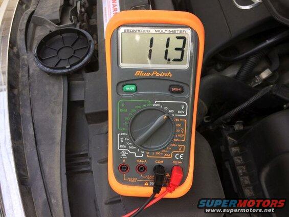 Multimeter showing 11.3 volts in a vehicle engine bay.