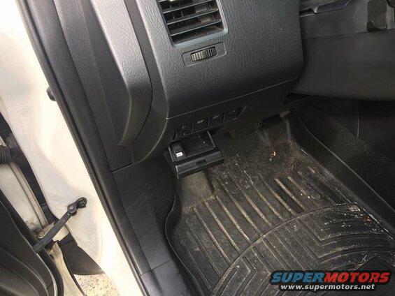 Interior of a white vehicle showing the dashboard and floor mat with a brake controller.
