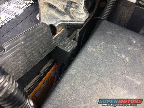 Close-up of a black HELLA automotive relay near a car battery.