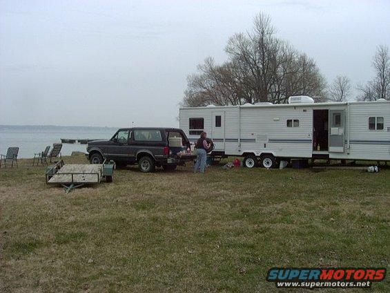 1992 Ford Bronco parked next to a large RV at a campsite by the water