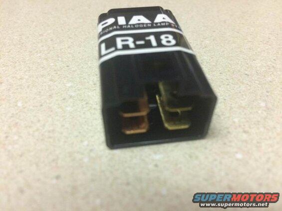Black PIAA LR-18 relay with brass connectors on a speckled surface.