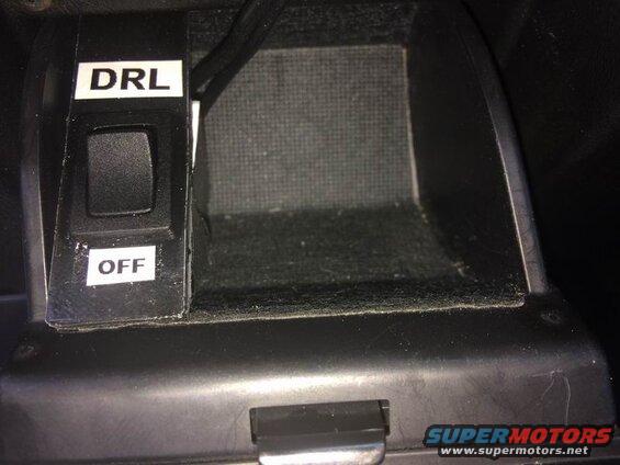 Close-up of DRL/OFF switch in a car's center console next to a storage compartment.