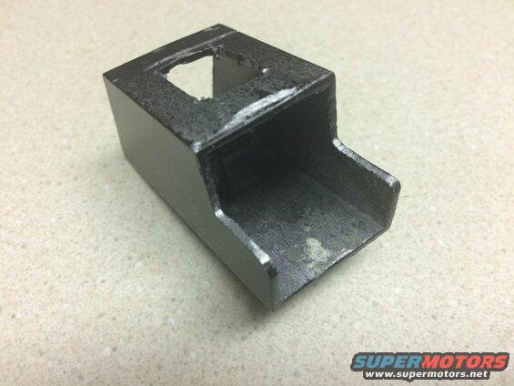 Dark gray metal part with a cut-out opening on a speckled surface.