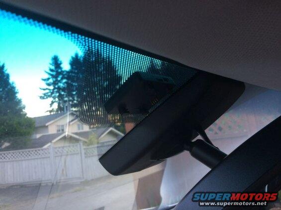 Interior view of car windshield with dashcam and houses outside.
