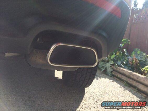 Close-up of a dark SUV's rear bumper and rectangular exhaust tip with chrome trim.