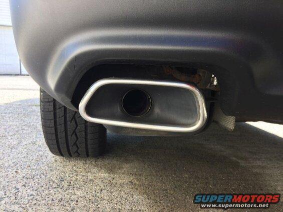 Close-up of a car's chrome oval exhaust tip on a black bumper.