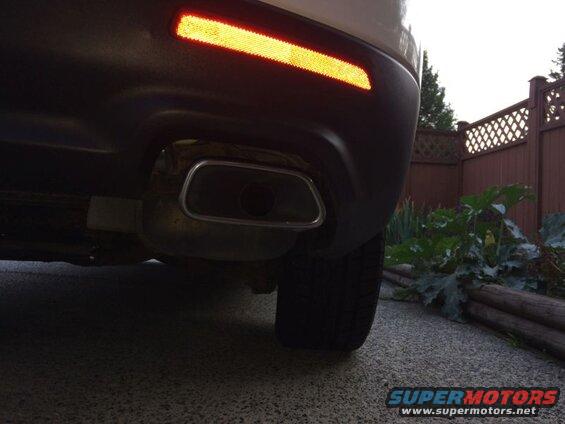 Rear view of a white SUV showing exhaust tip and red reflector on bumper.