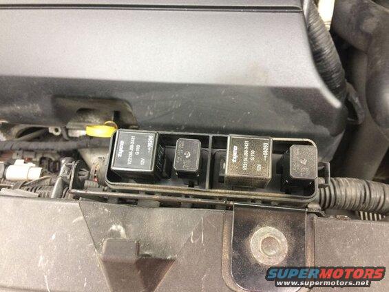 Close-up of automotive relays in a fuse box under a vehicle hood.