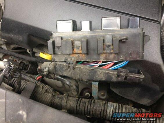Vehicle fuse box with relays and colorful wires in the engine bay.