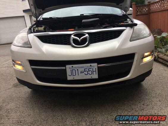 White Mazda CX-9 front view, hood open, hazard lights on.