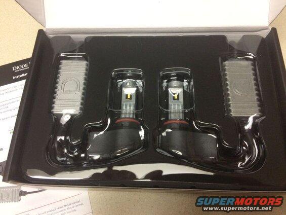 Four LED headlights in a black plastic box with a white cardboard insert.
