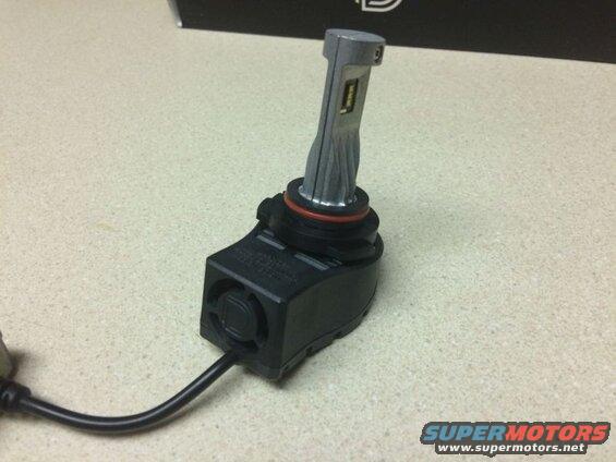 LED headlight bulb with black base and silver heatsink on a speckled countertop.