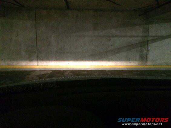 Headlights illuminating a concrete wall in a parking garage.