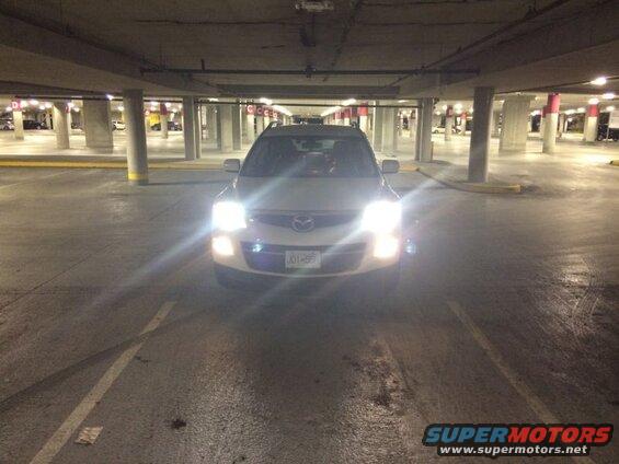 White 2009 Mazda CX-9 SUV with headlights on in a parking garage.