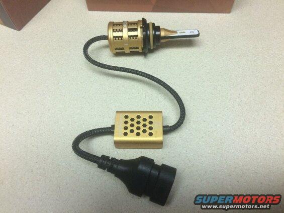 Gold LED headlight bulb assembly with black braided wire and connector on speckled countertop.