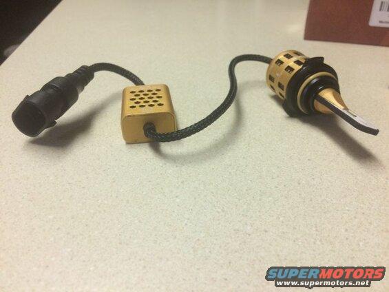 Gold LED headlight bulb with black connector and gold heat sink on a speckled countertop.