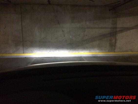Vehicle headlights shining on a concrete wall in a parking garage.