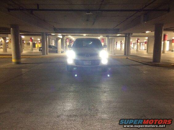 White SUV with headlights on in a parking garage