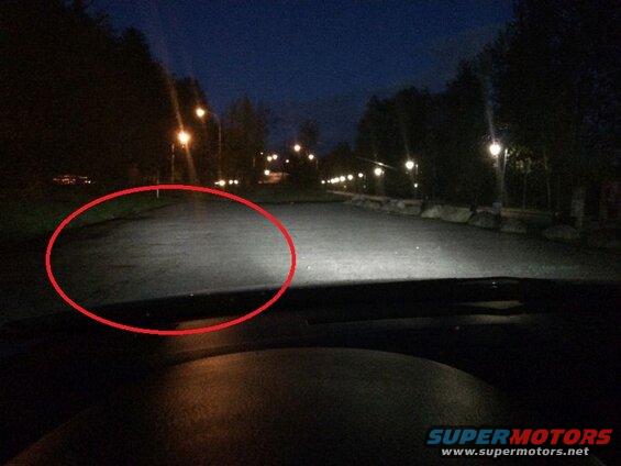 View from inside a vehicle at night looking at a wet road and streetlights.