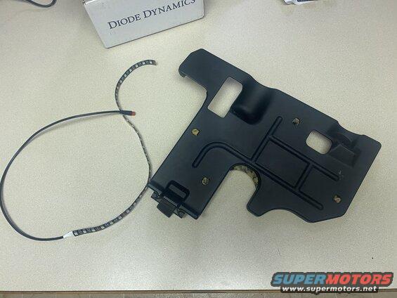 Black plastic underbody panel with LED strip lights on a table.