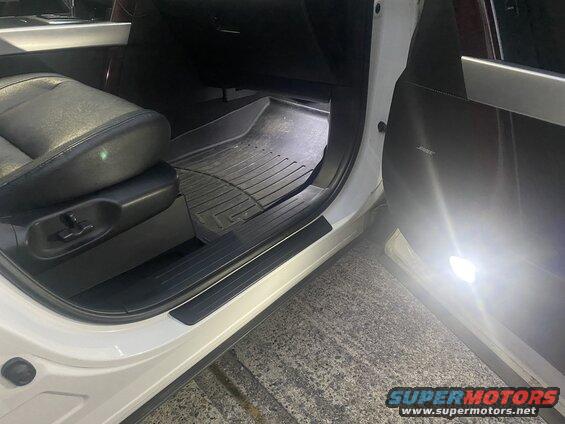 Interior of a white SUV showing driver's seat, floor mat, and illuminated door.