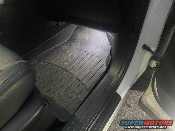 Close-up of a black rubber floor mat inside a vehicle, with a leather seat visible.