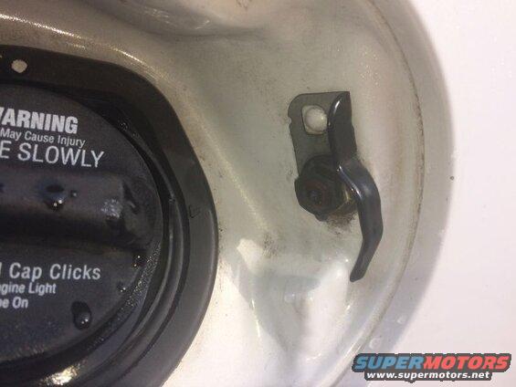 Close-up of a vehicle's fuel filler neck with a black fuel cap and a lever.