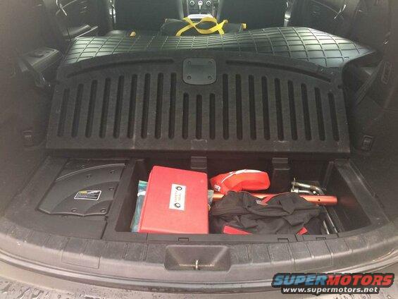 Open trunk of a dark SUV with storage bins holding a red safety kit and orange rods.