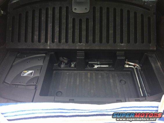 Open trunk of a vehicle showing storage compartment with spare tire and jack tools.