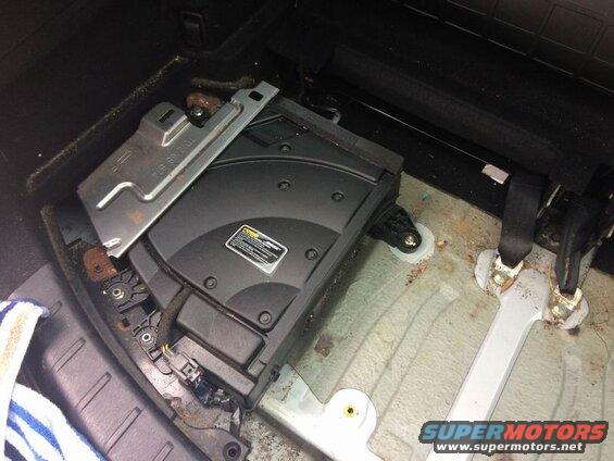 Interior view of a vehicle showing a removed subwoofer, seatbelt anchors, and floor.