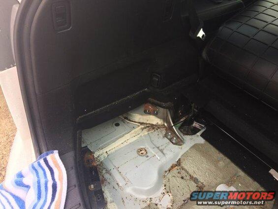 Interior of a vehicle cargo area with floor removed, showing rust and debris.